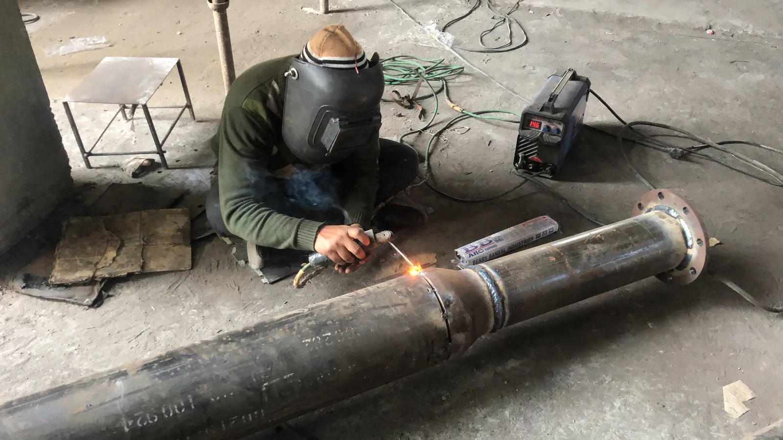 Welder fabricating a flanged branch on a mild steel water pipe