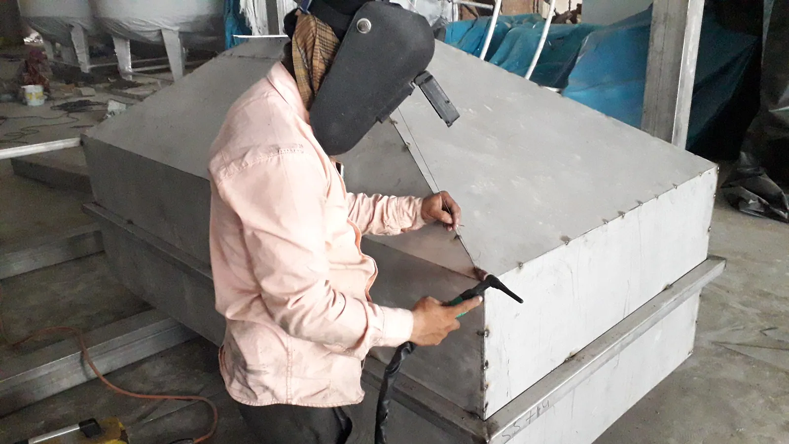 Worker finishing a fabricated rectangular stainless steel tank